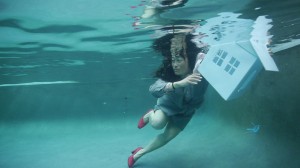 Debby Kajiyama holds a miniature house underwater. She wears a business suit.