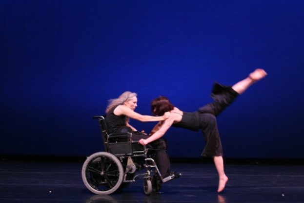 Younger dancer pushes towards dancer in wheelchair