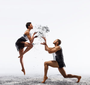 two dancers facing one another sprinkling dark matter mid-air