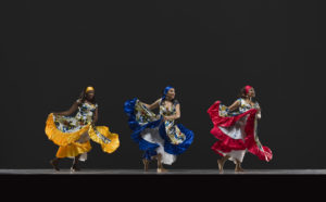 three female Cuban dancers in brightly colored dresses and headbands
