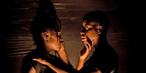 two dancers caressing each other's faces in a dim room
