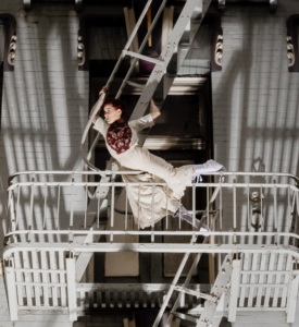 woman in cream-colored dress with red hair dancing on a fire escape