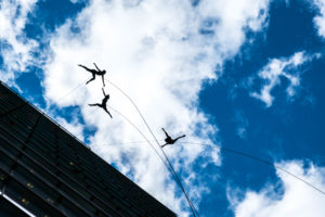 Three vertical dancers jumping away from the side of a building.