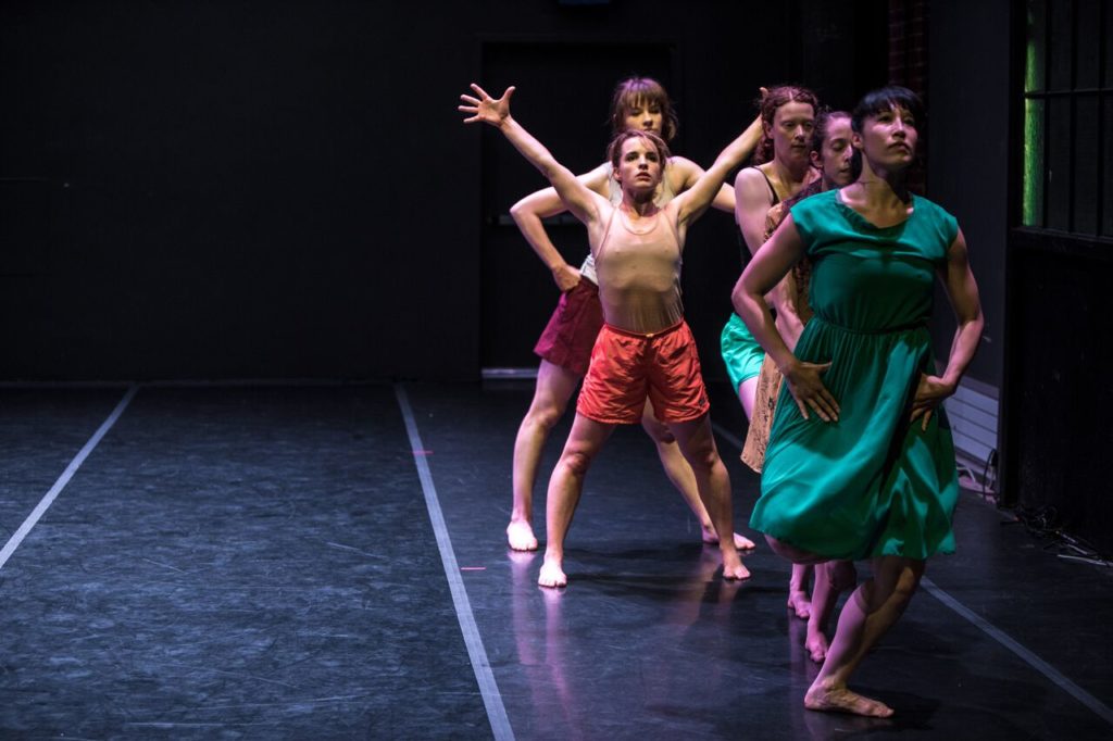 Five dancers standing in various poses in a crooked line.