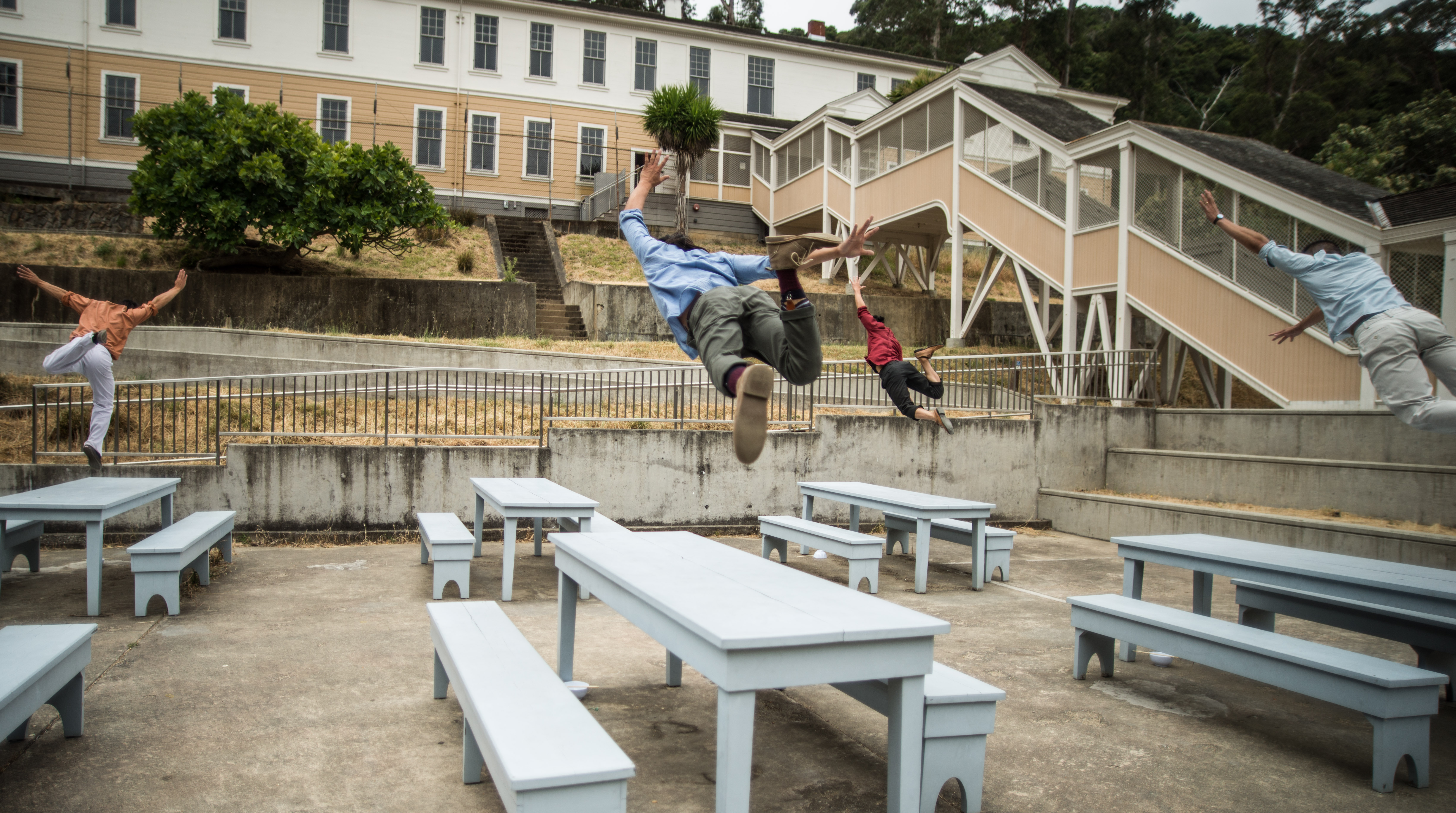 Four dancers outside at the Angel Island’s Immigration Station hurdling over lunch tables.