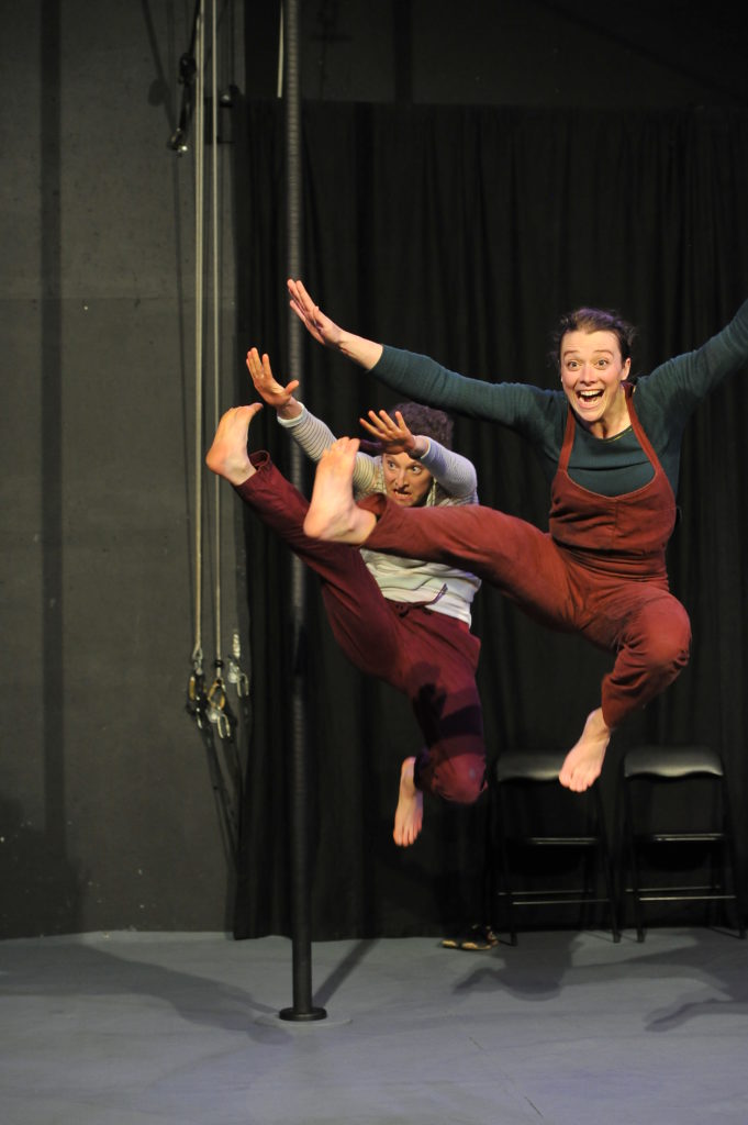 Two people jumping with one leg extended to the side and arms reflecting the legs. Faces are animated and happy.