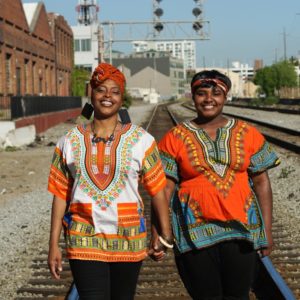 Two people holding hands, smiling, and standing on train tracks