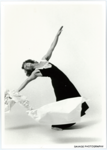 Black and white studio shot of Terry Sendgraff in a dark dress arching back with one arm aloft and the other holding a piece of fabric
