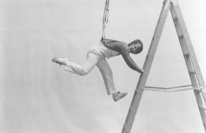 Terry Sendgraff suspended in mid-air by a harness and holding onto a rung partway up a ladder