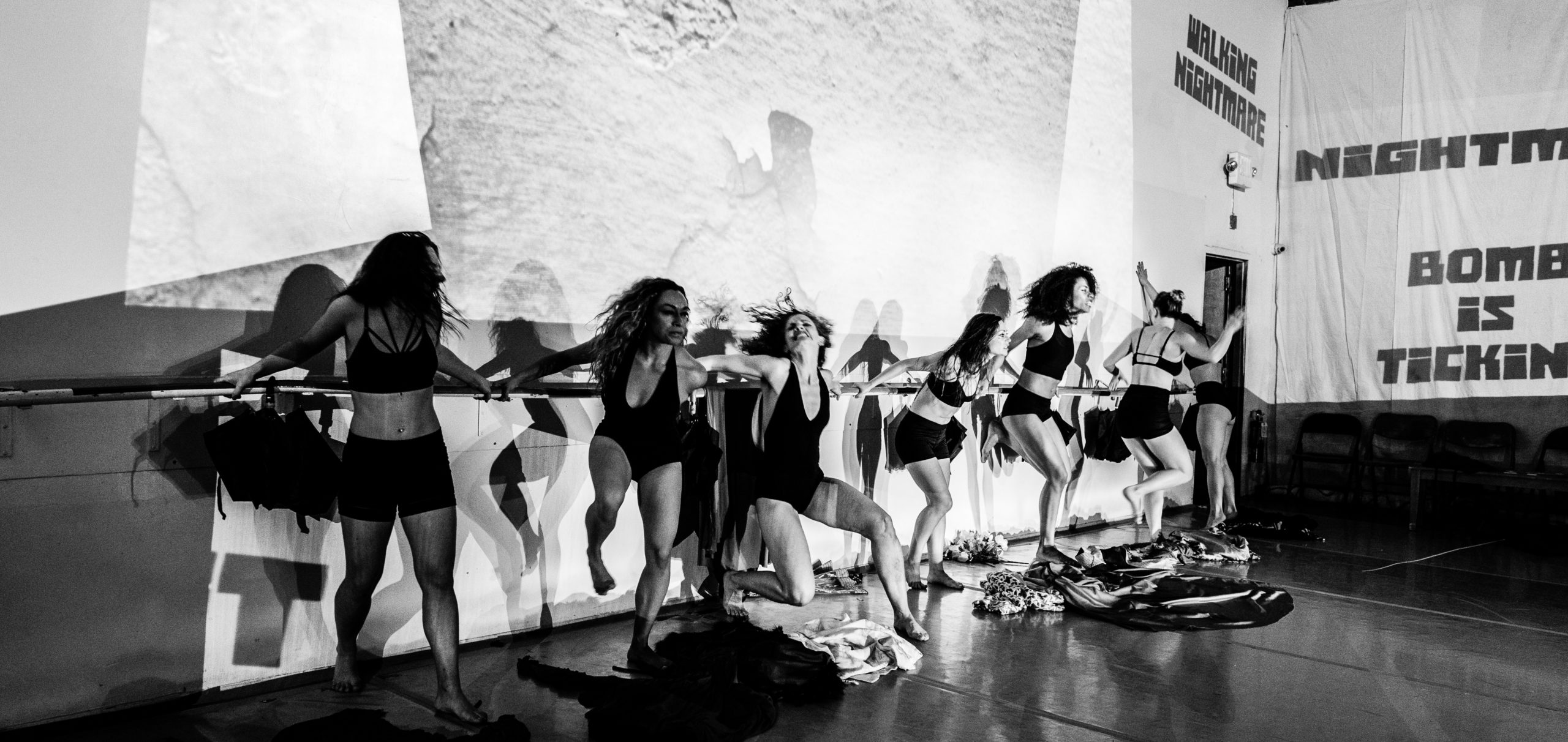 Black and white image of women lined up against a ballet bar