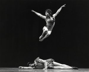 Dancer leaping over another who is laying down on the floor