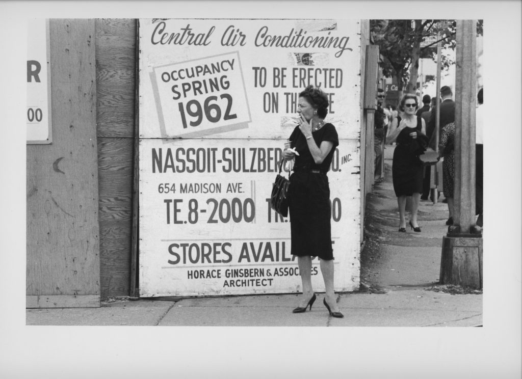 Woman smoking in front of a sign that says "Occupancy Spring 1962"