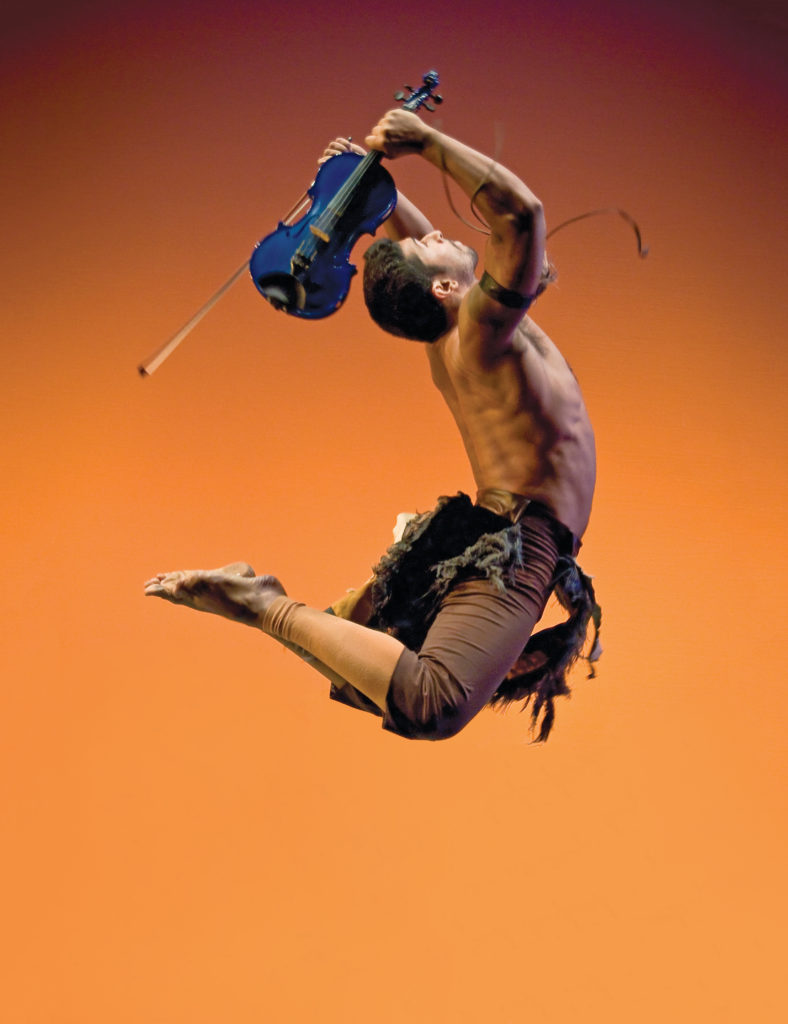 Quetzal Guerrero jumps mid-air with a violin raised above his head