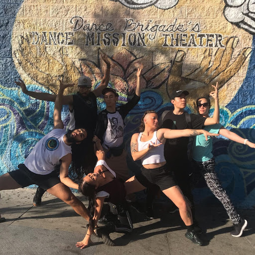 Group of dancers posing in front of a mural that says "Dance Brigade's Dance Mission Theater"