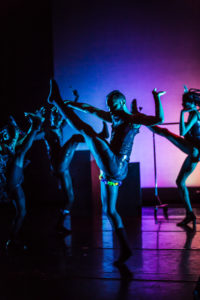 Performance shot of KnowShade Vogue dancing on a dimly lit stage