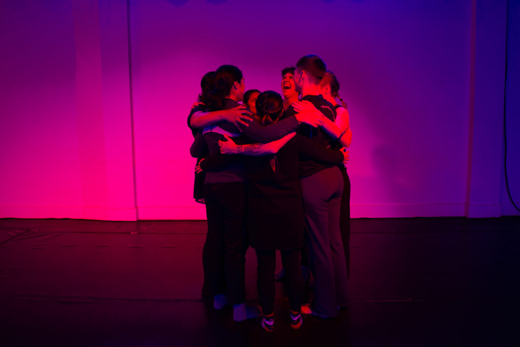 Group of dancers on stage embracing one another