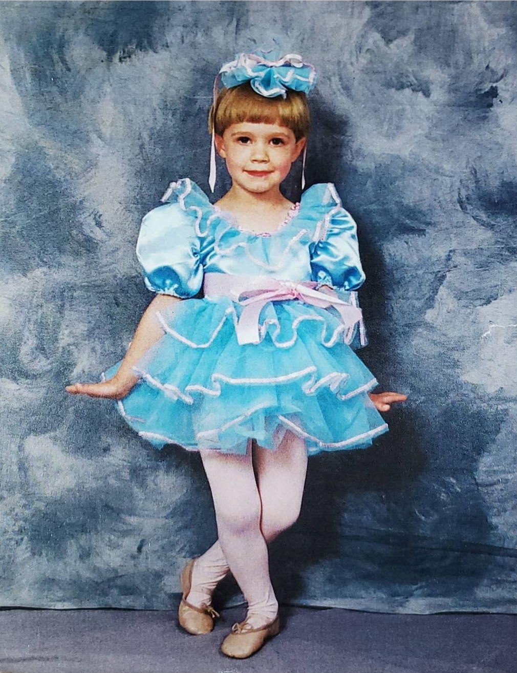 The author Julia Davidson as a young dancer, in a blue tutu, curtseying and looking straight at the camera.