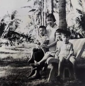 A black and white photo of a Chinese mother sitting on a bench with her three young children.