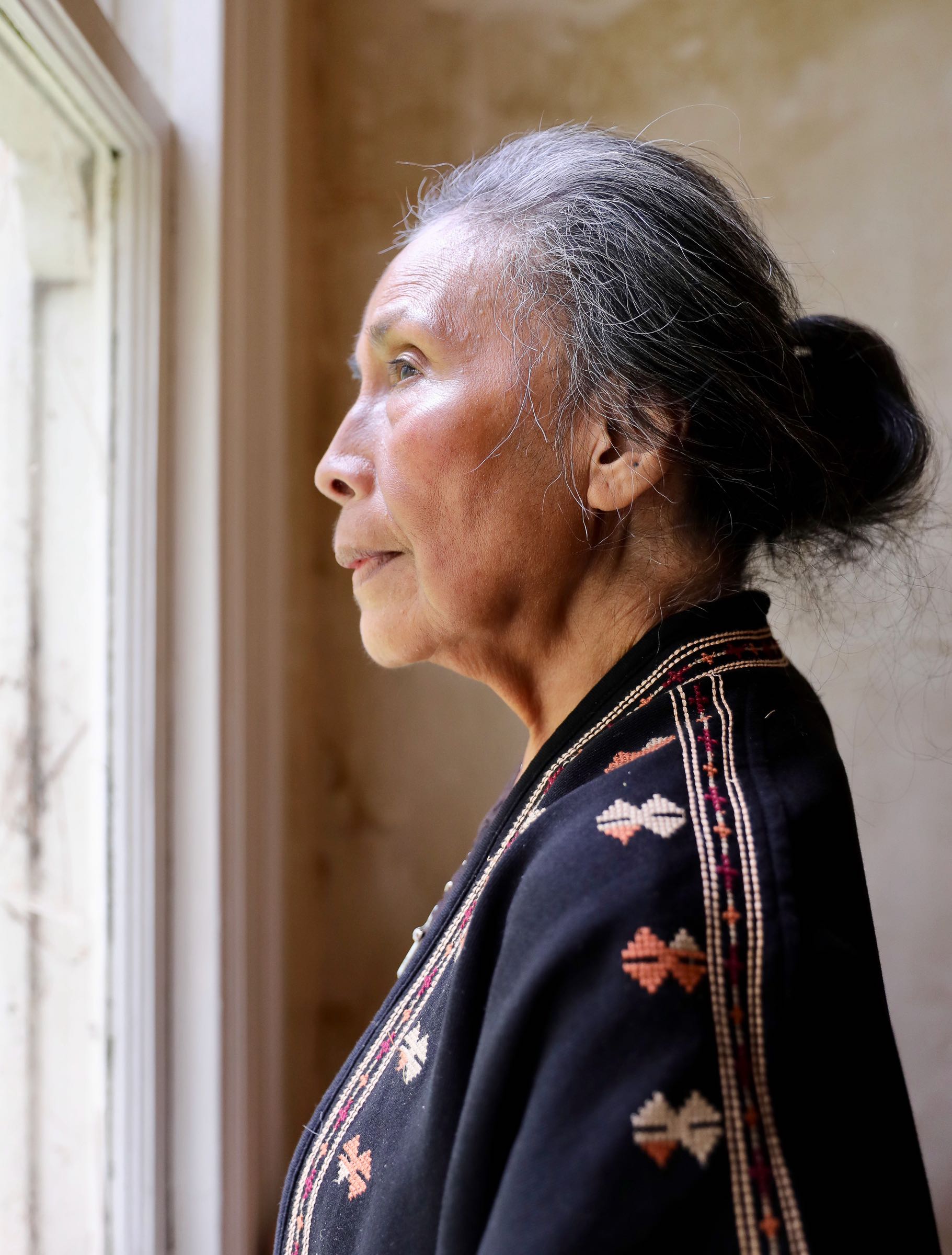 Panching, an elder Filipina, looks out a window of a historic house at Fort Barry with a contemplative look.