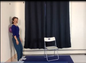 Screenshot from an online class that shows Diana Lara pushing a small inflatable ball that is placed between her shoulder blades against a wall to provide awareness to the upper torso.