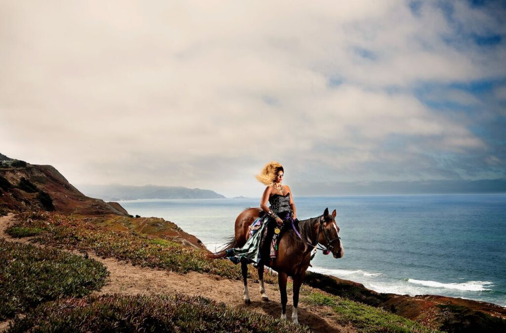 DJ Emancipation riding a horse down a hill by the ocean.