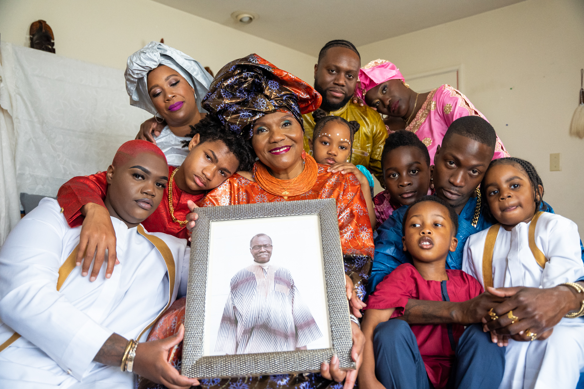 A group photo showing three generations of a family close together and holding a framed photo.