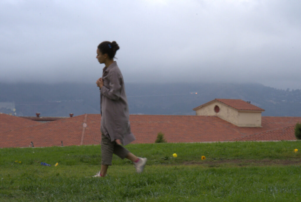 A somewhat blurred image of Audrey walking in the grass at Fort Mason, the San Francisco fog in the background