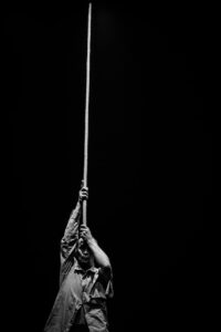 Shinichi holding a single stick vertically. Black and white photo.