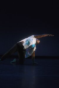 A female dancer performs on a dimly lit stage.