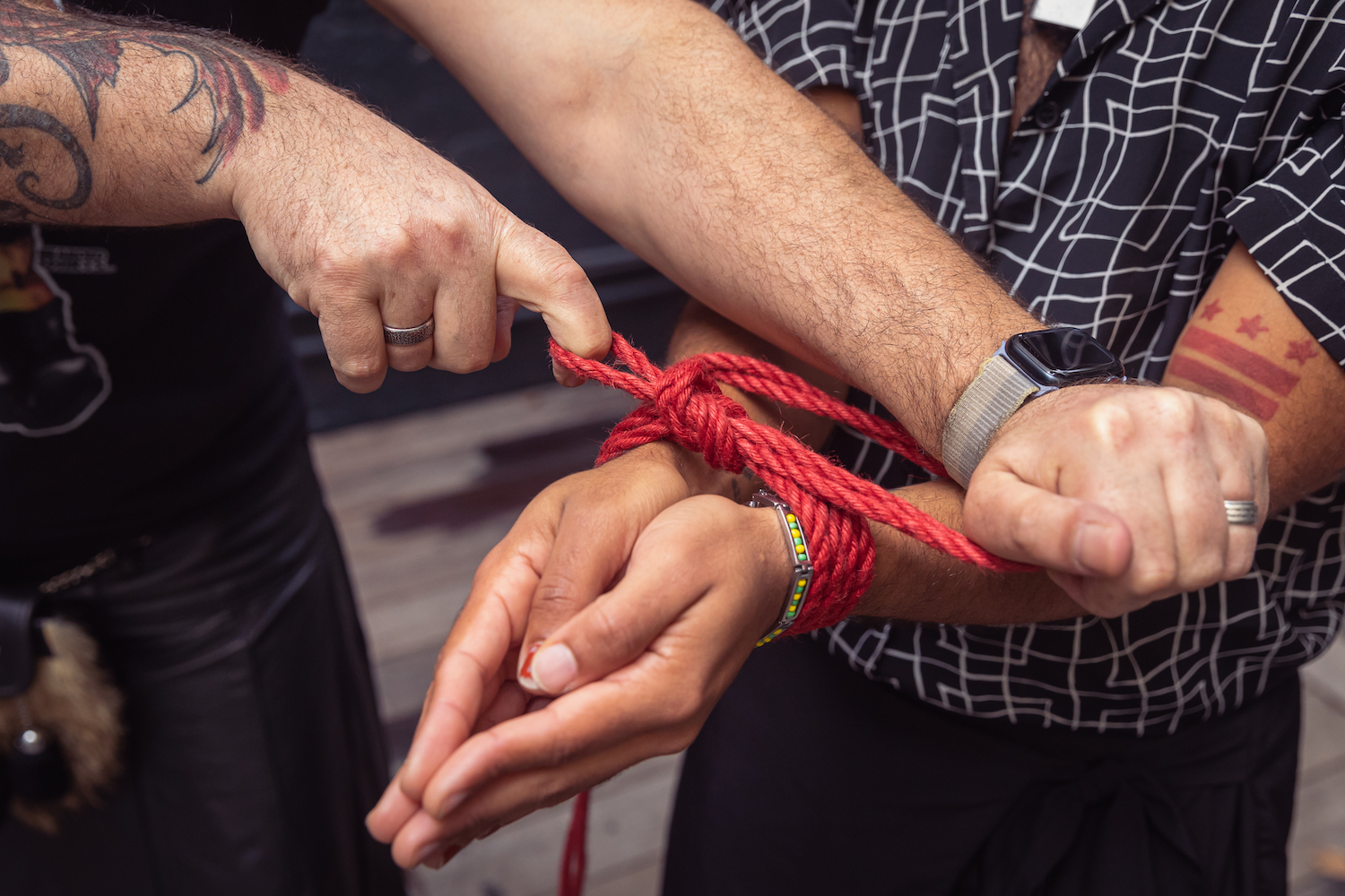 A man in the act of tying a rope in a knot around the wrists of another man.