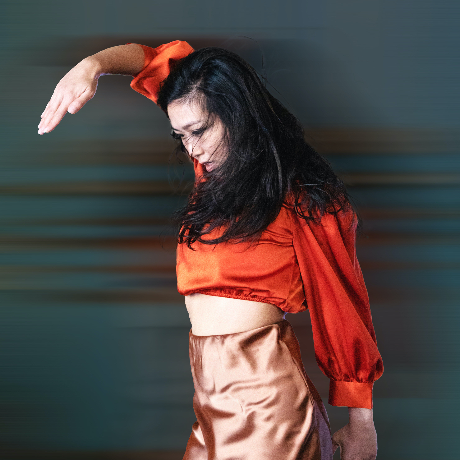 dancer in orange with a focused gaze and raised arm