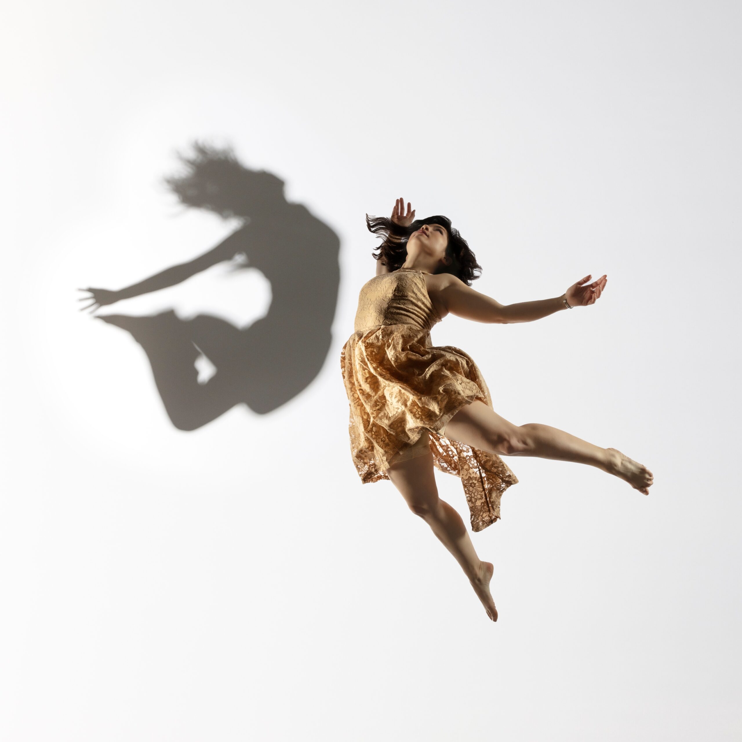 Megan Lowe jumps into the air with her back arched, arms and legs reaching behind her. The shadow of Shira Yaziv is floating above her.
