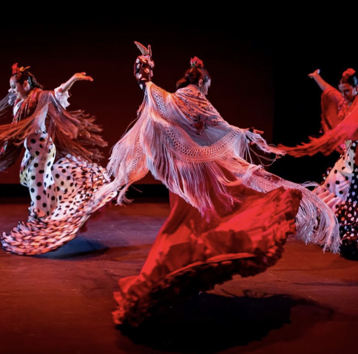 Three dancers dance in flamenco costumes