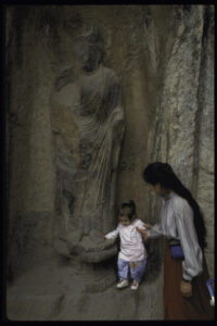 Old film photo of toddler Melissa with Joy in front of Buddha sculpture in Asia
