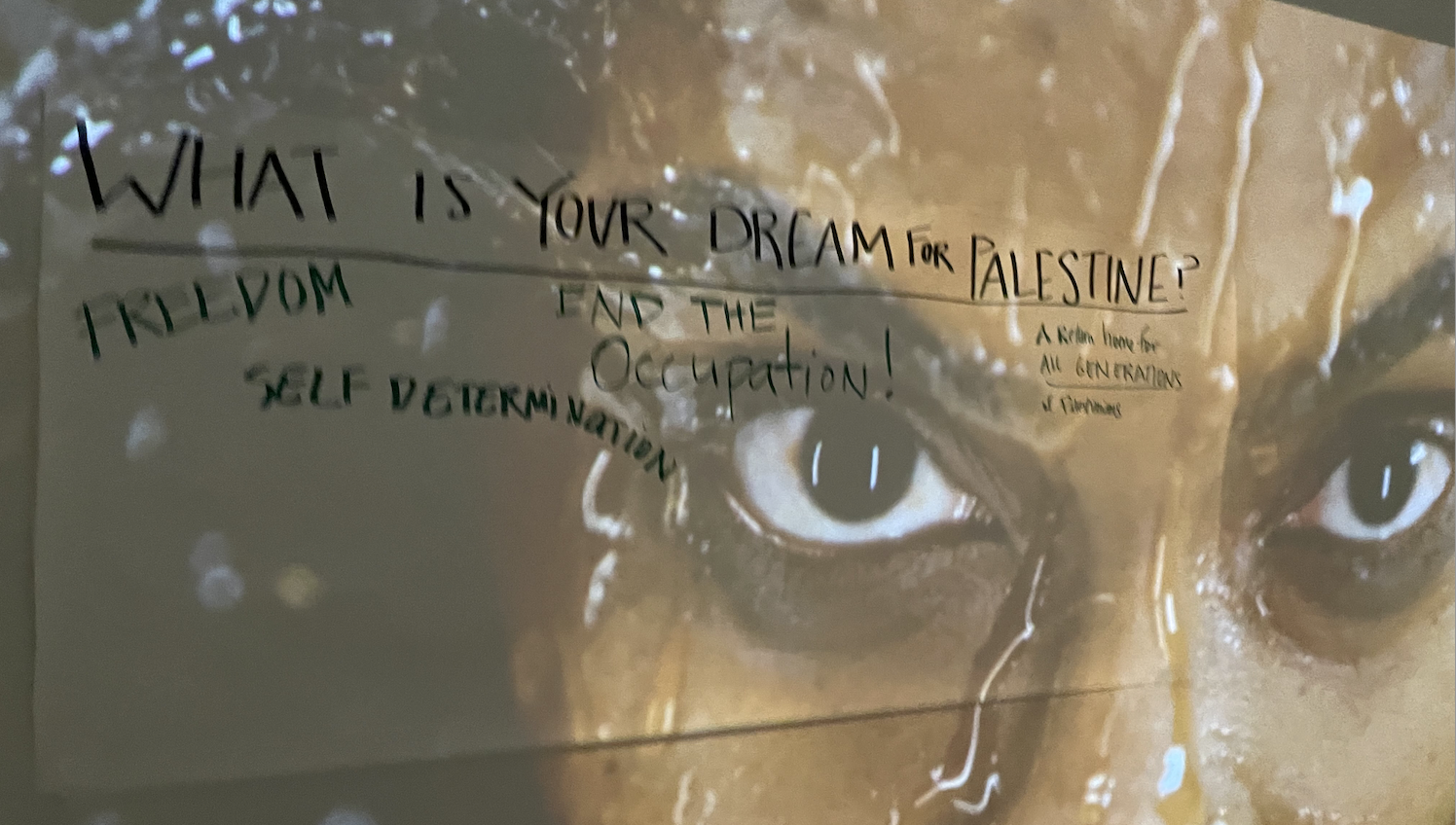 Installation featuring the face of a woman of African descent covered in honey. Words on paper over it read "What is your dream for Palestine?"