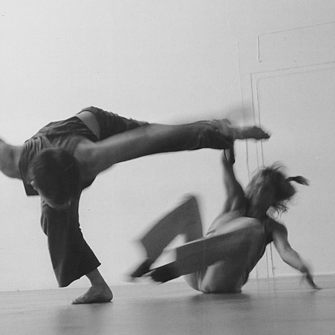 Black-and-white photo: two dancers move in a studio space.