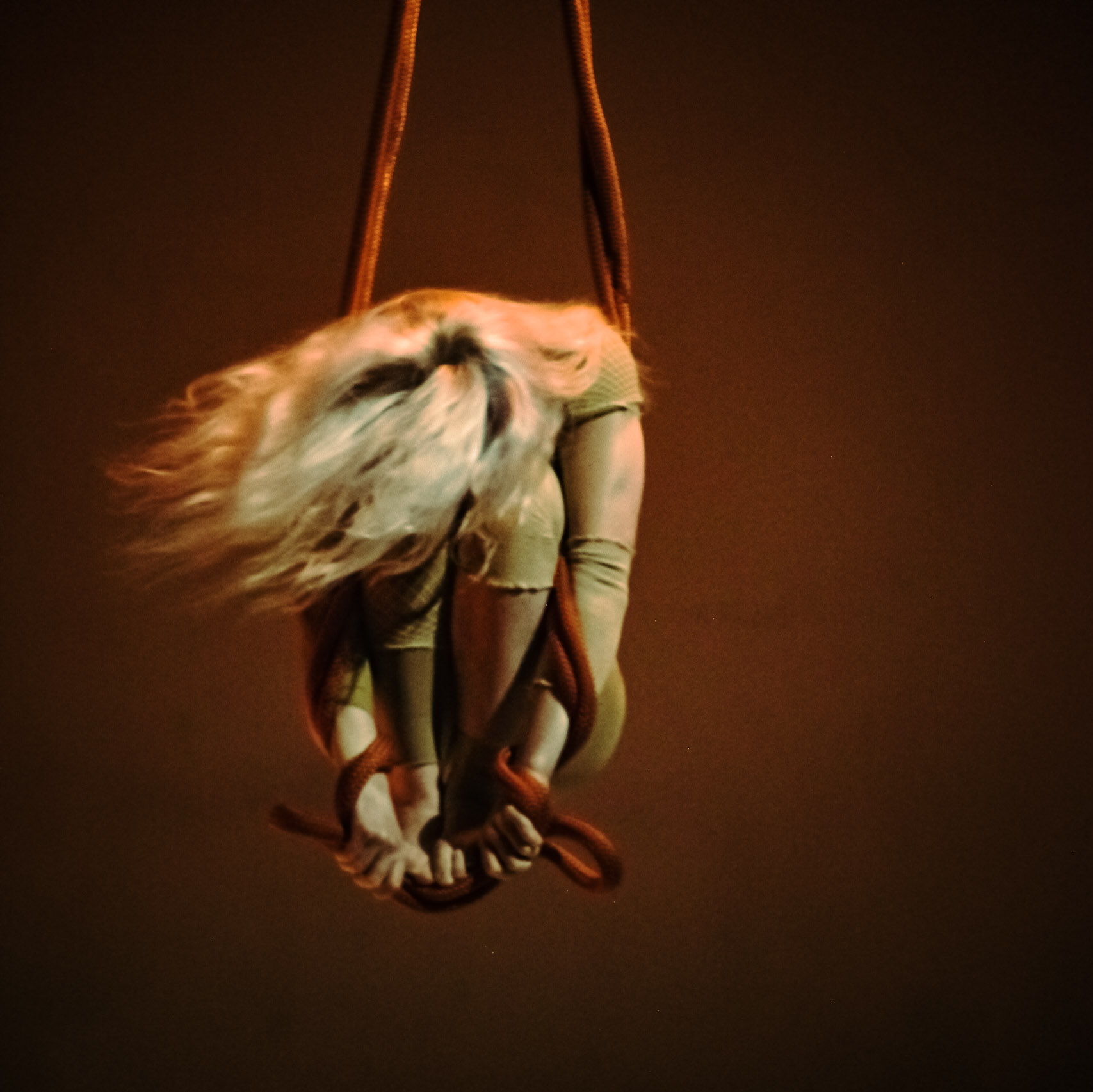 An aerialist spins on red rope loops.