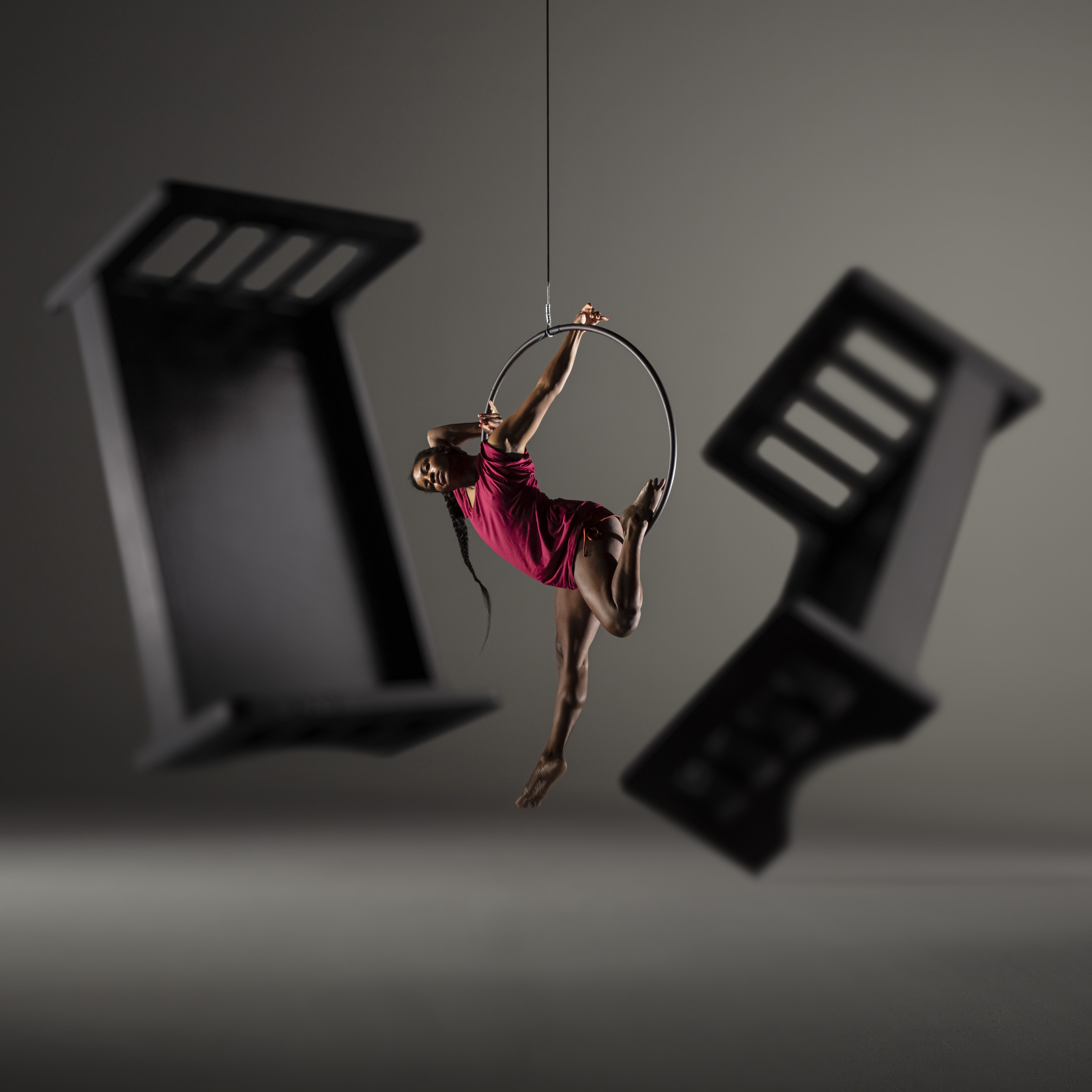 A dancer suspends from a hoop with bed frame shadows behind her