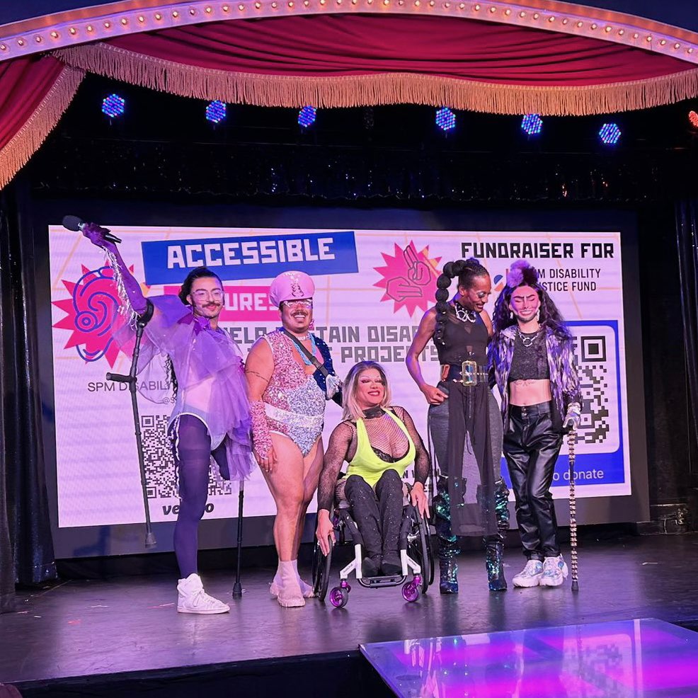 Photo of Accessible Futures cast posing on stage together in colorful outfits in front of a screen showing the Accessible Futures logo. 