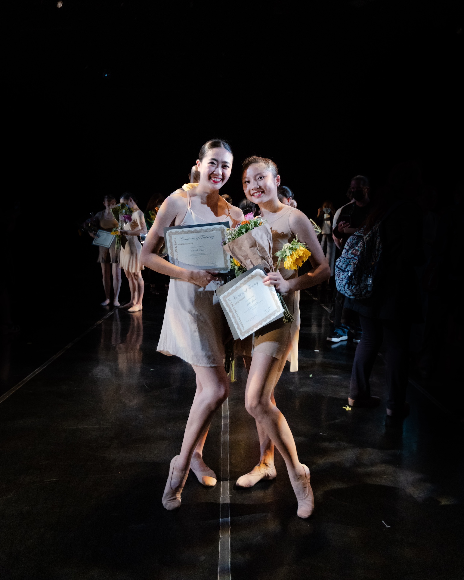 Two dancers pose onstage with flowers and certificates.