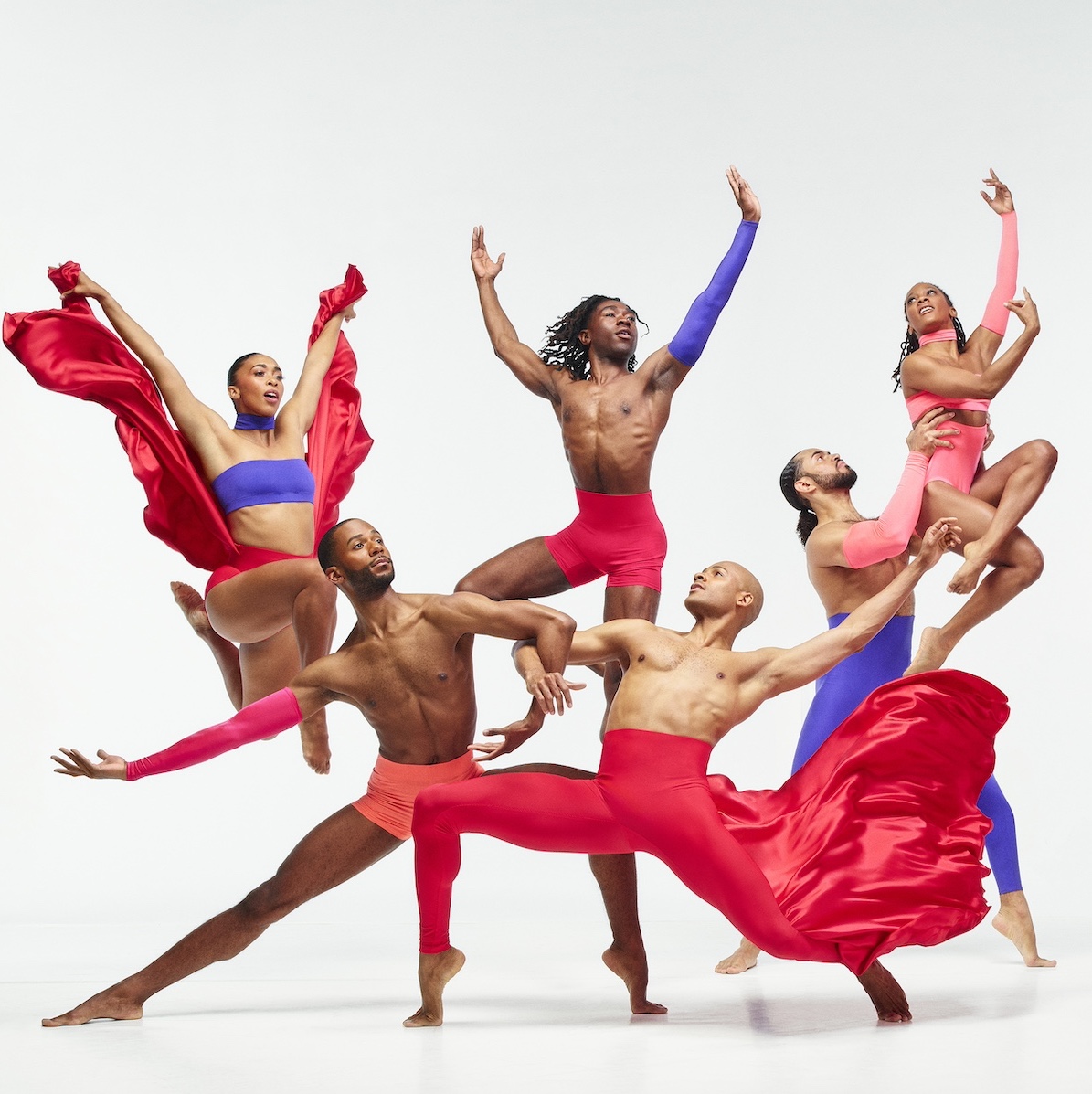 Six Alvin Ailey dancers wear pink and purple clothing and stand in a dynamic pose.