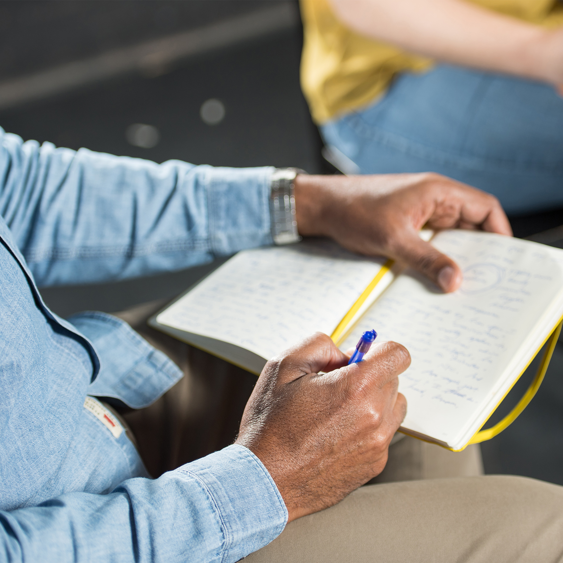 A dancer writes in a notebook with a blue pen while seated. 