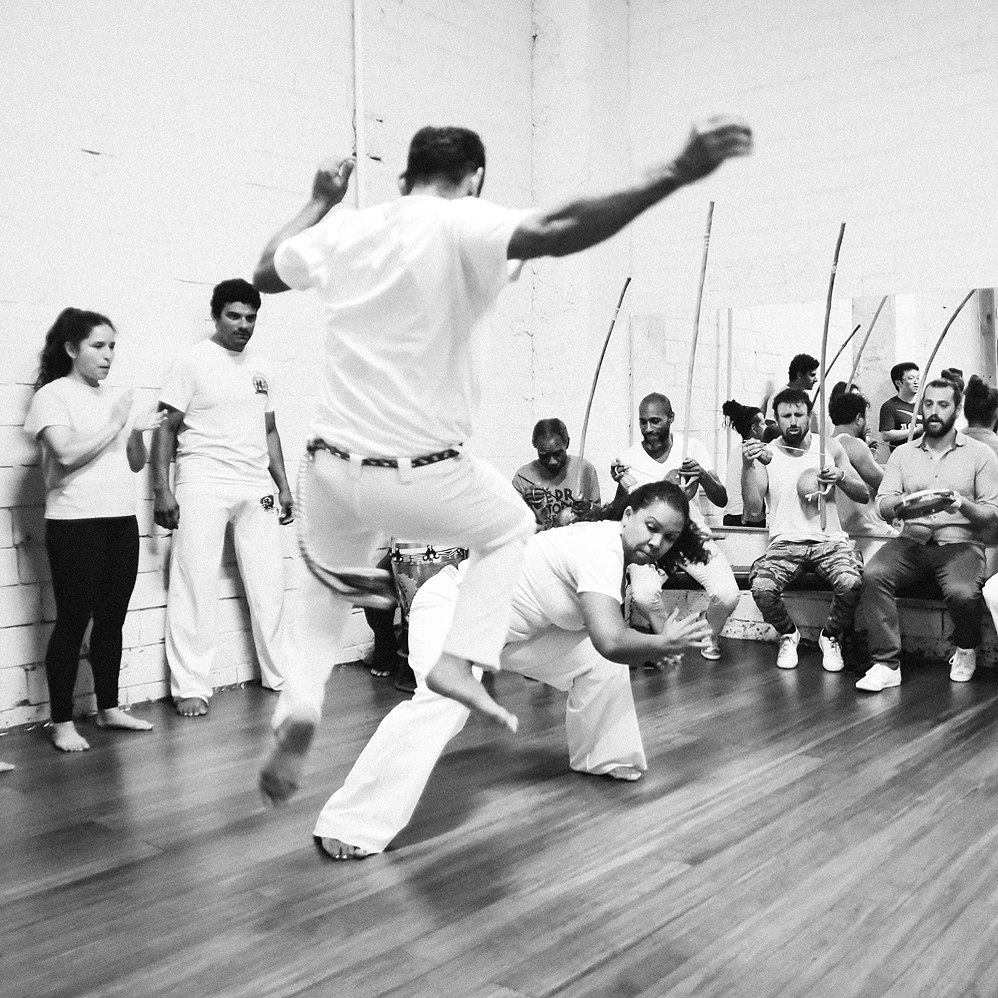 Capoeira roda: Two people playing capoeira flanked by other people playing music and singing.