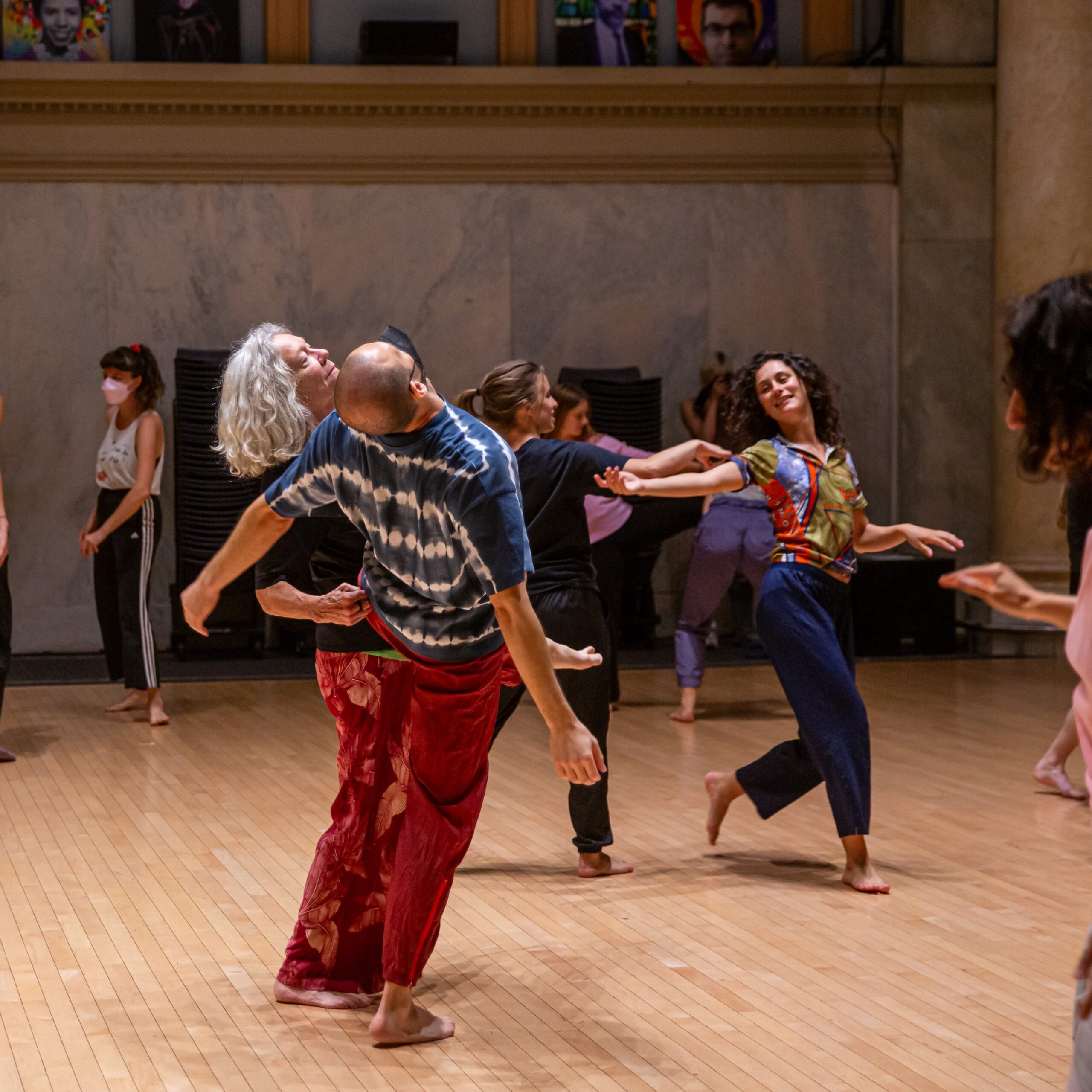 A group of dancers partner in a dance studio with a light wooden floor.