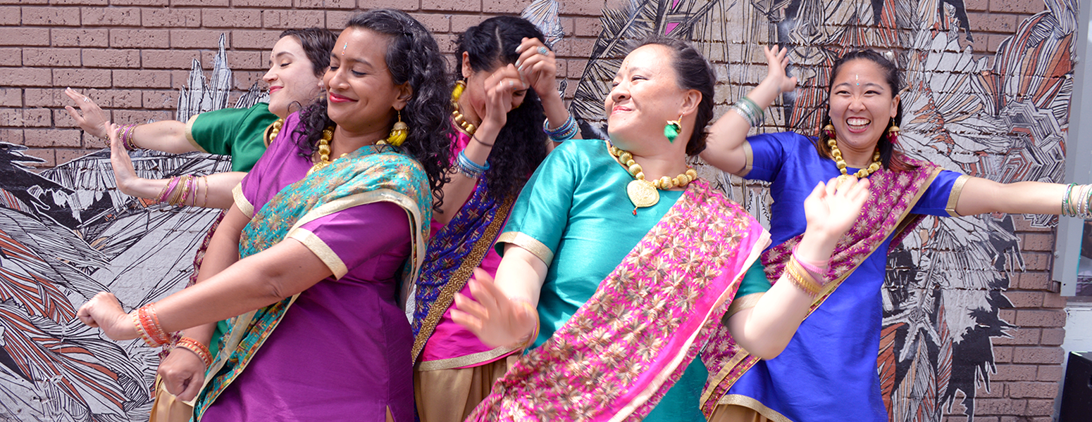 five dancers in brightly colored clothing dancing in front of a mural