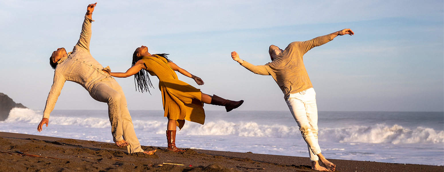 Three dancers on a beach wearing neutral colors