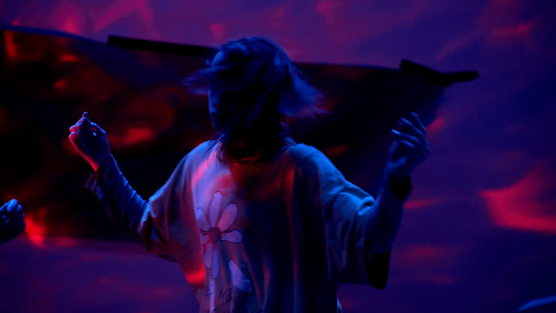 A dancer twirls their head with their arms up saturated in blue red light 