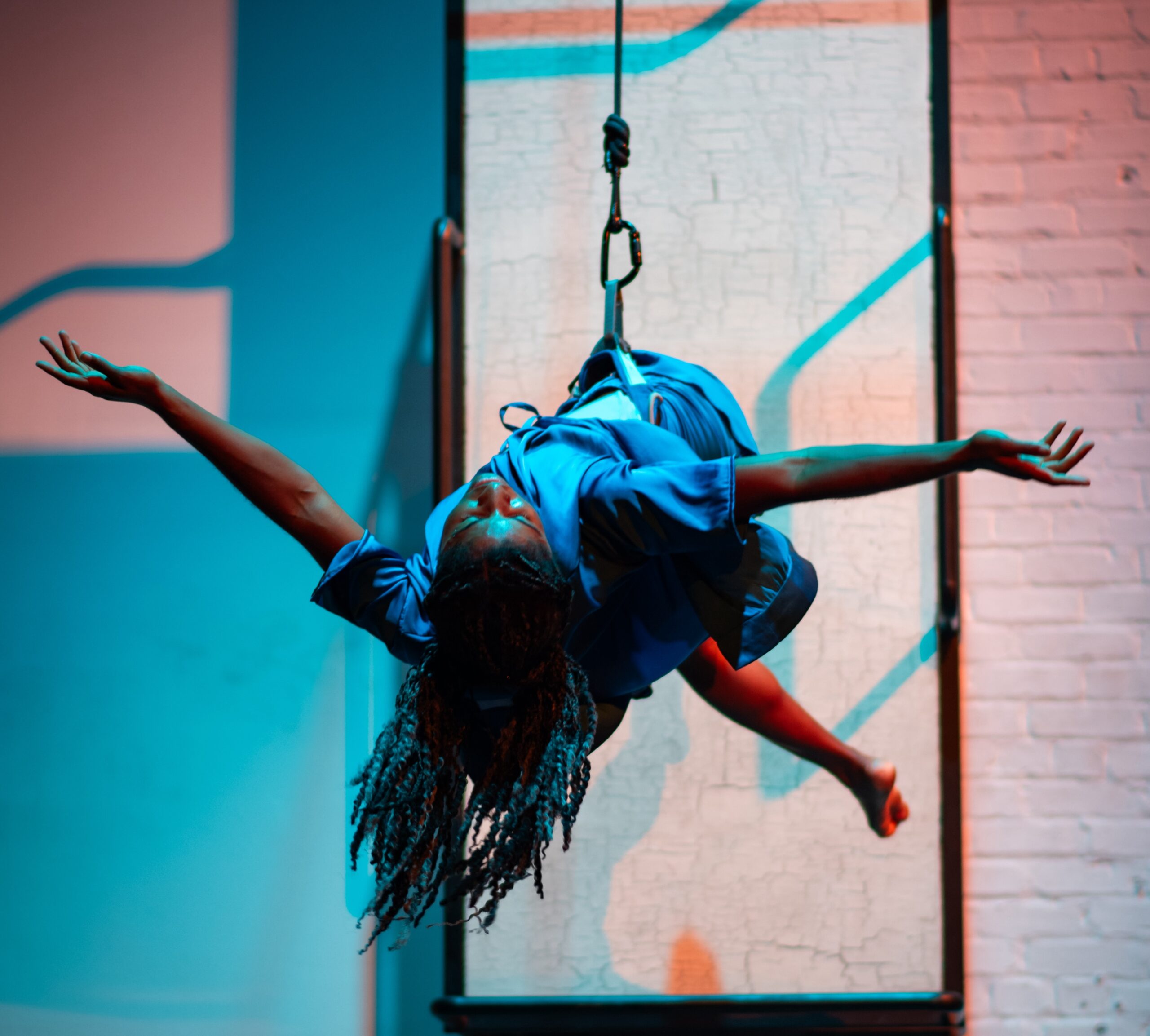 Black female bodied dancer in blue silk costume suspended and floating  in front of a mounted steel bed