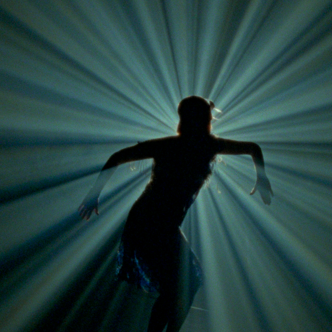 Silhouette of a person with outstretched arms against radiating light beams.