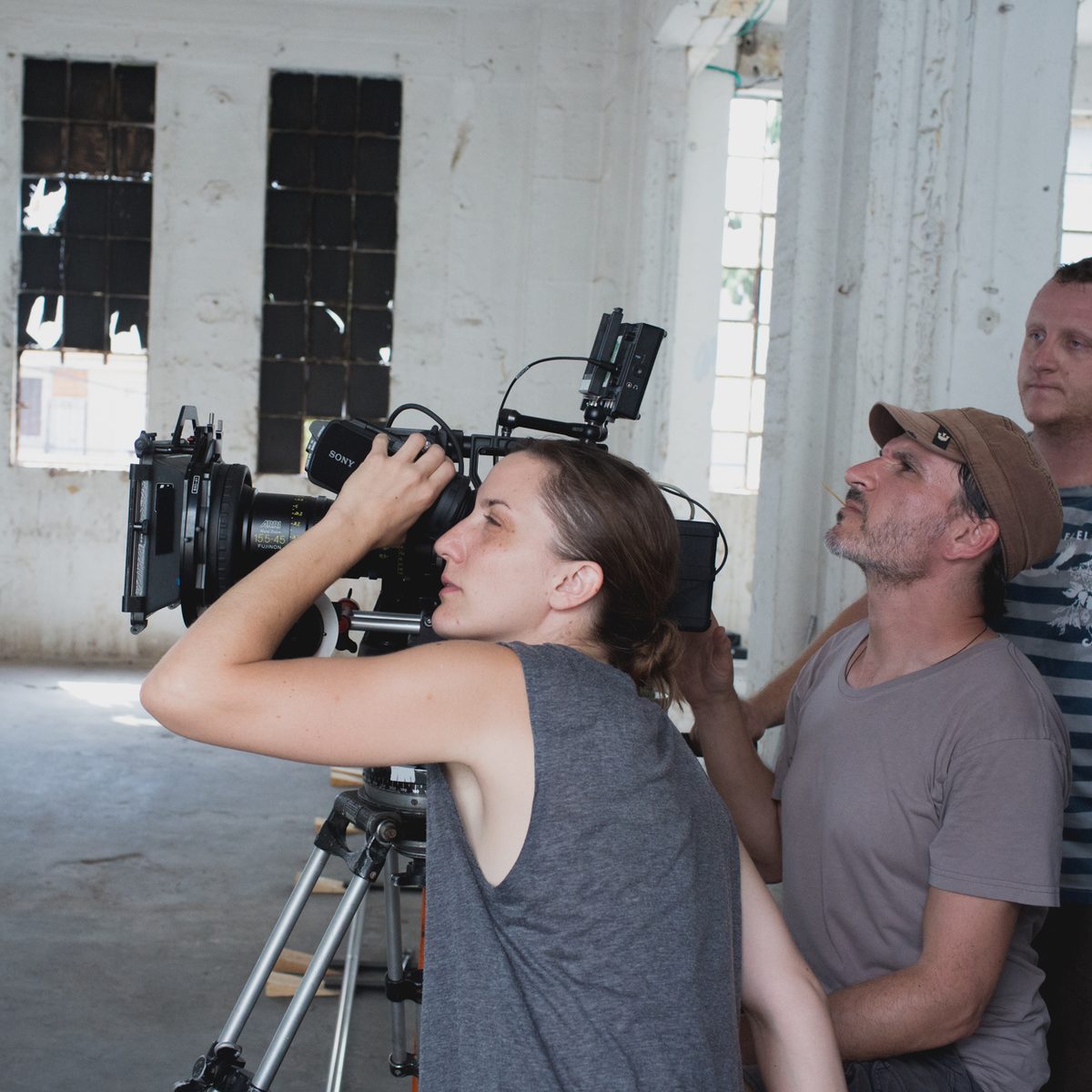 Three people working together in a large, dimly lit room with a mounted camera.